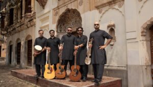 Five men stand next to each other holding musical instruments and dressed in all black